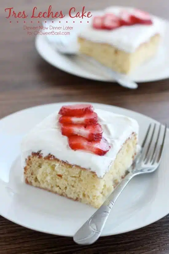 Slice of tres leches cake topped with whipped cream and strawberries on a plate with a fork.