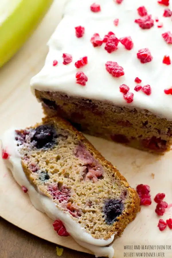 This super-soft and moist banana bread is exploding with a double-delight of juicy berries and perfectly covered in a tangy cream cheese icing. | dessertnowdinnerlater.com