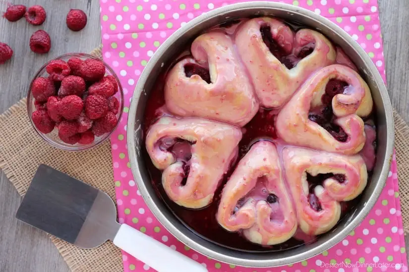 Glazed heart shaped rolls in pan with raspberries.