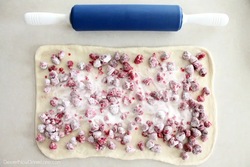 Dough rolled into a rectangle with sugar coated raspberries on top.