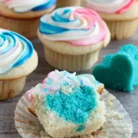 These Gender Reveal Cupcakes have pink, blue, and white swirled frosting on top that hides the secret colored heart in the center of the cupcake revealing the baby's gender when you bite into it! (Step-by-Step Photo Tutorial)