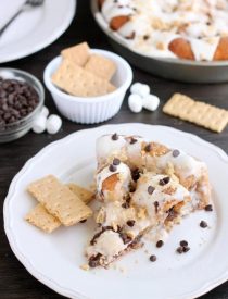 Crushed graham crackers, mini chocolate chips, and mini marshmallows are rolled up in buttery cinnamon sugar rolls to create this S'mores Cinnamon Roll Cake. Top it all off with a marshmallow frosting and extra toppings for a delicious dessert!