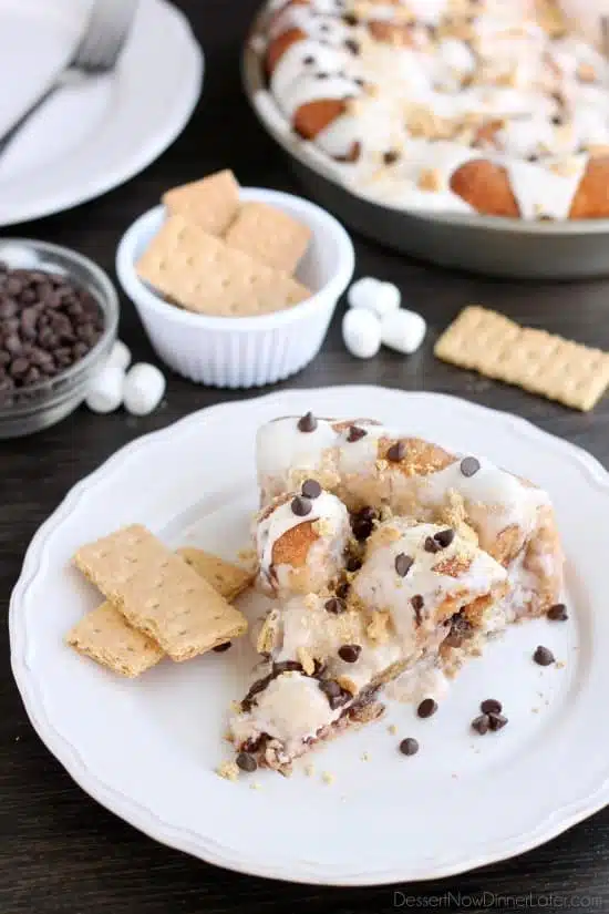 Crushed graham crackers, mini chocolate chips, and mini marshmallows are rolled up in buttery cinnamon sugar rolls to create this S'mores Cinnamon Roll Cake. Top it all off with a marshmallow frosting and extra toppings for a delicious dessert!