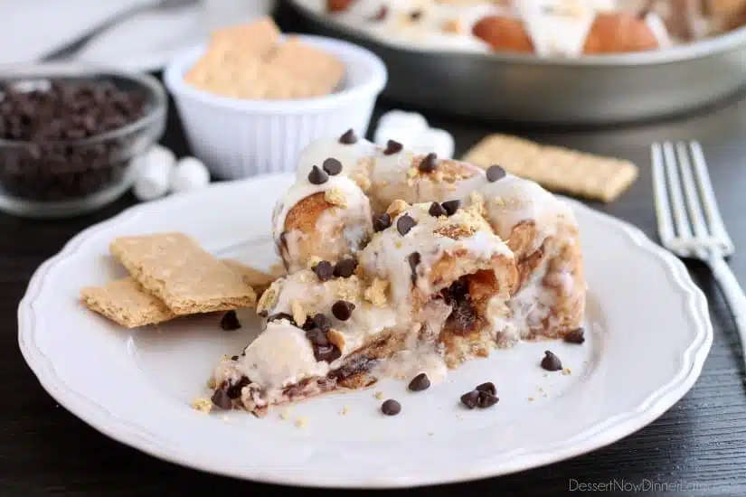 Crushed graham crackers, mini chocolate chips, and mini marshmallows are rolled up in buttery cinnamon sugar rolls to create this S'mores Cinnamon Roll Cake. Top it all off with a marshmallow frosting and extra toppings for a delicious dessert!