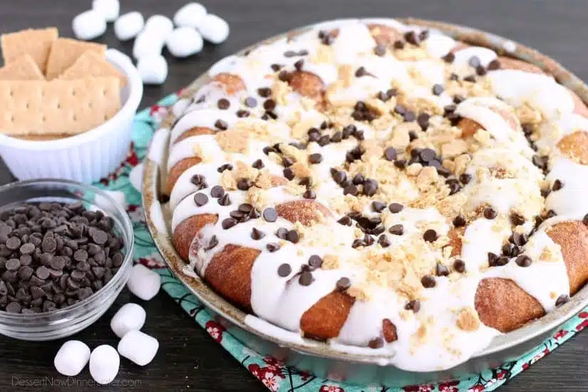 Crushed graham crackers, mini chocolate chips, and mini marshmallows are rolled up in buttery cinnamon sugar rolls to create this S'mores Cinnamon Roll Cake. Top it all off with a marshmallow frosting and extra toppings for a delicious dessert!