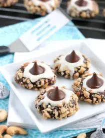 Chocolate cookie dough is rolled in nuts and topped with buttercream and chocolate kisses to create these thick and chewy Chocolate Cream Thumbprint Cookies.