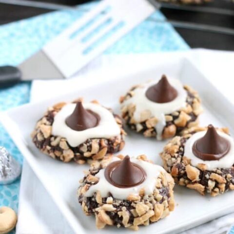 Chocolate cookie dough is rolled in nuts and topped with buttercream and chocolate kisses to create these thick and chewy Chocolate Cream Thumbprint Cookies.