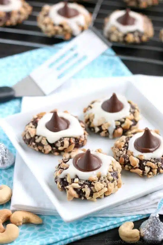 Chocolate cookie dough is rolled in nuts and topped with buttercream and chocolate kisses to create these thick and chewy Chocolate Cream Thumbprint Cookies.