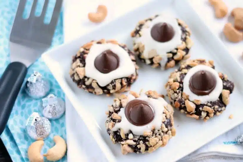 Chocolate cookie dough is rolled in nuts and topped with buttercream and chocolate kisses to create these thick and chewy Chocolate Cream Thumbprint Cookies.