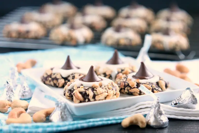 Chocolate cookie dough is rolled in nuts and topped with buttercream and chocolate kisses to create these thick and chewy Chocolate Cream Thumbprint Cookies.