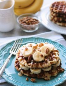 Cinnamon Roll Waffles are topped with freshly sliced bananas, crunchy nuts, and a maple cream cheese drizzle.