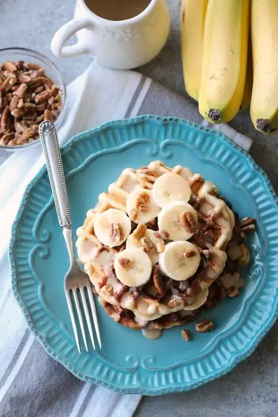 Cinnamon Roll Waffles are topped with freshly sliced bananas, crunchy nuts, and a maple cream cheese drizzle.