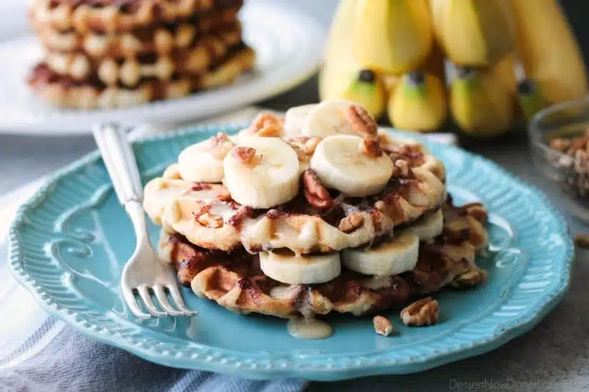 Cinnamon Roll Waffles are topped with freshly sliced bananas, crunchy nuts, and a maple cream cheese drizzle.