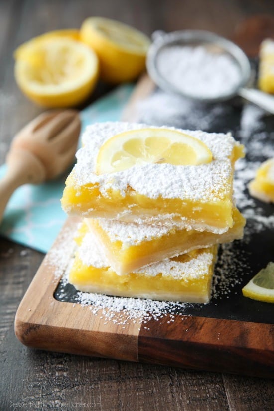 Three lemon bars stacked with powdered sugar and a lemon slice on top.