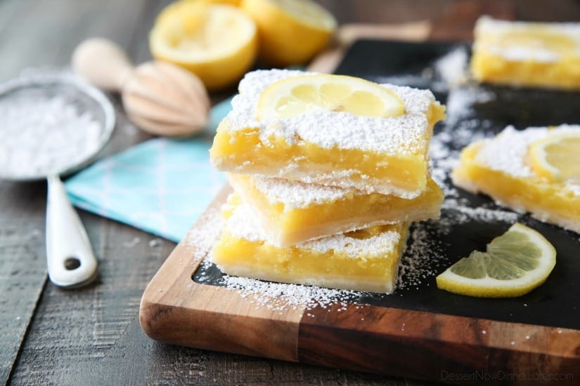 Three lemon bars stacked with powdered sugar and a lemon slice on top.