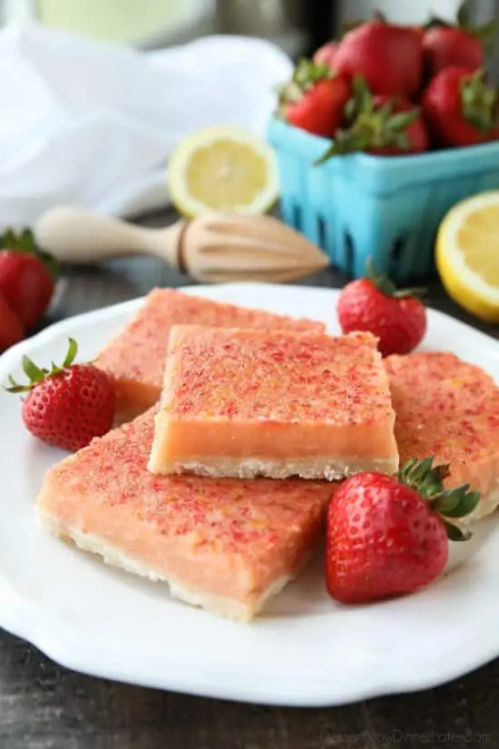 Squares of strawberry lemon bars on plate with fresh strawberries.