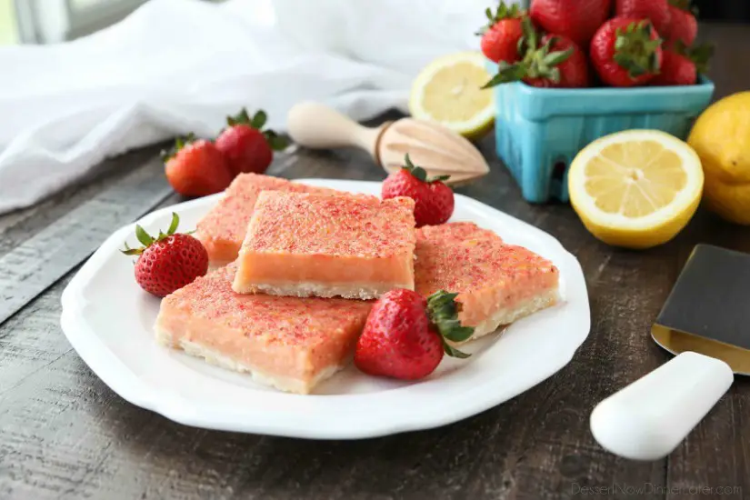 Squares of strawberry lemonade bars on plate with fresh strawberries.