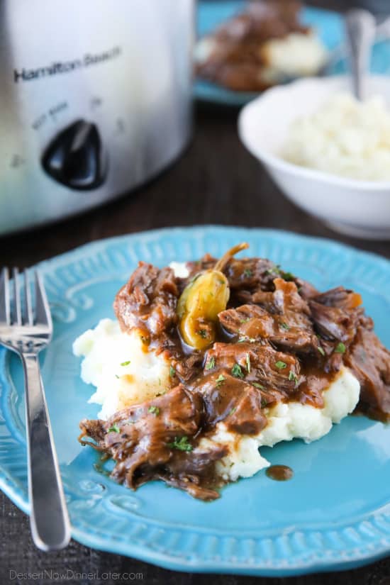 Plate of mashed potatoes topped with Mississippi Pot Roast shredded beef in gravy.