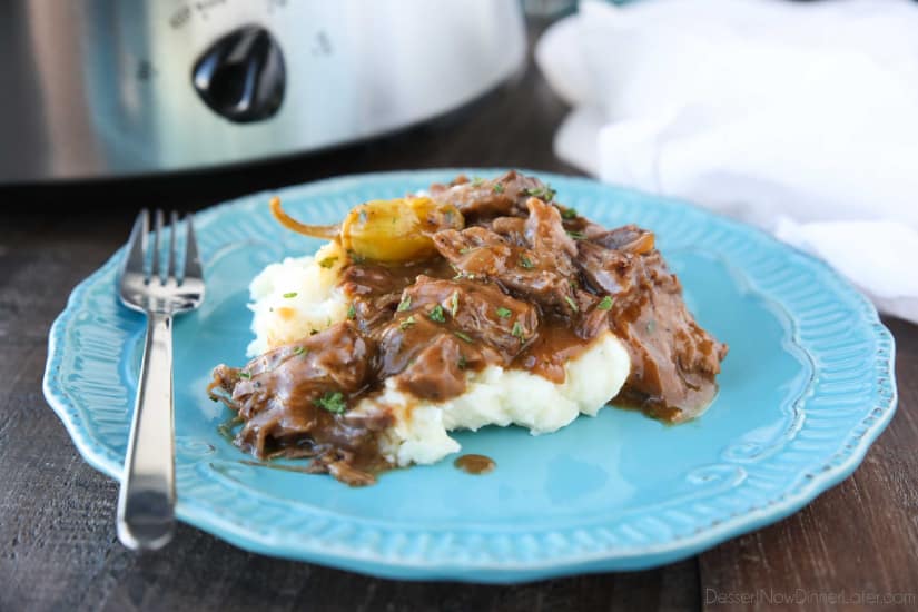 Plate of mashed potatoes topped with Mississippi Pot Roast shredded beef in gravy.