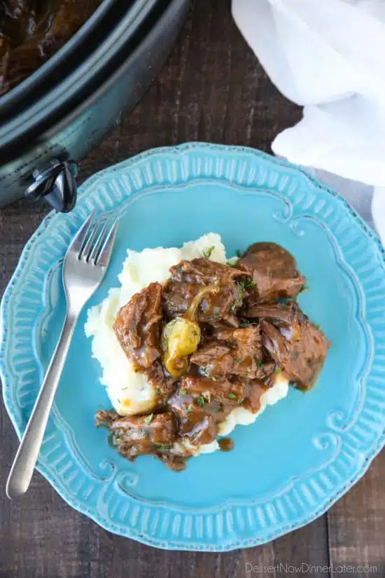 Plate of mashed potatoes topped with Mississippi Pot Roast shredded beef in gravy.