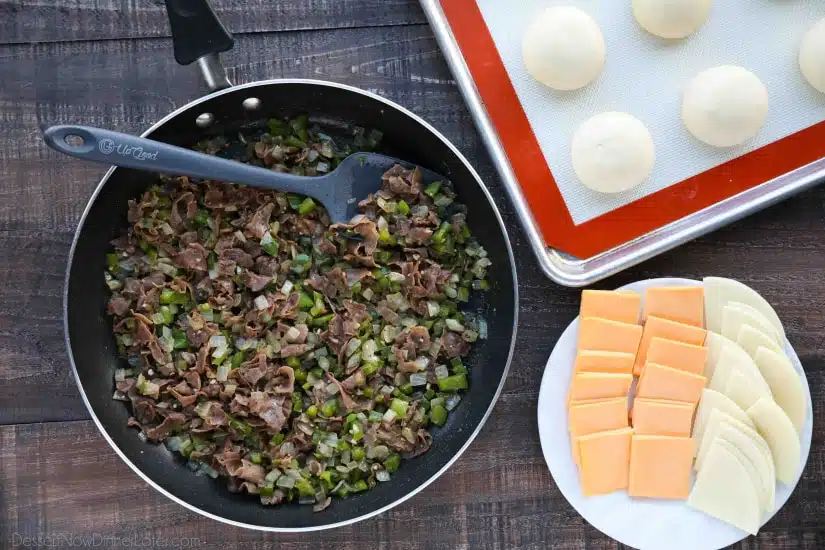 Skillet with cooked meat and vegetables next to a plate of sliced cheese.