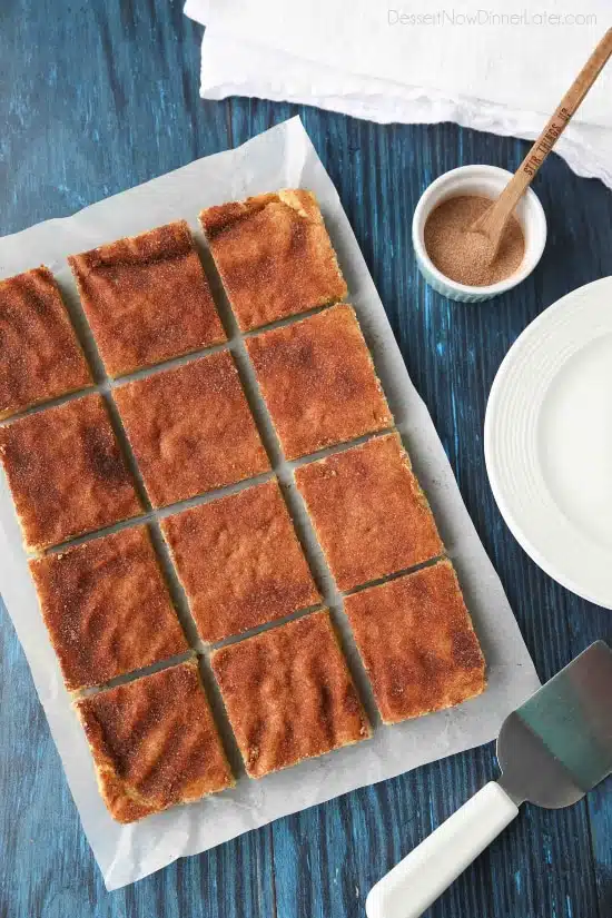 Snickerdoodle Bars transform classic snickerdoodle cookies into easy-to-make blondies. Thick, soft, buttery cookie bars are topped with plenty of cinnamon-sugar. These flavorful, melt-in-your-mouth dessert bars make enough to serve a crowd. Perfect for potlucks, picnics, and parties.