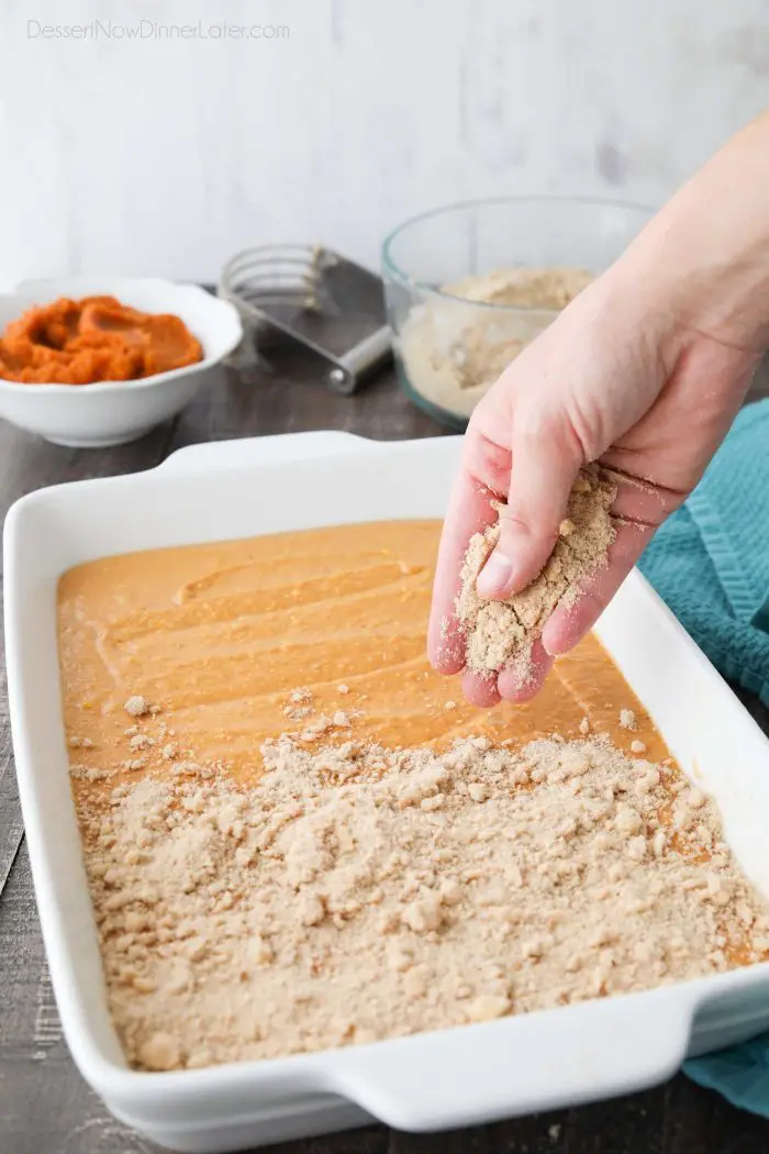 Sprinkling crumb streusel on top of pumpkin cake batter.