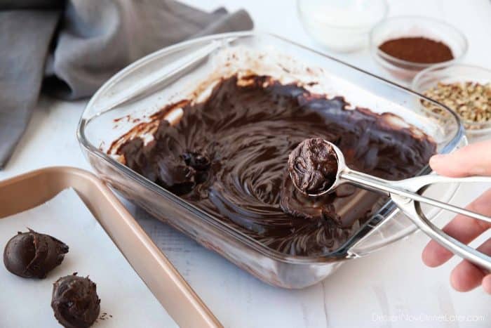 Chilled chocolate ganache is scooped for truffles and placed on a tray with parchment paper.