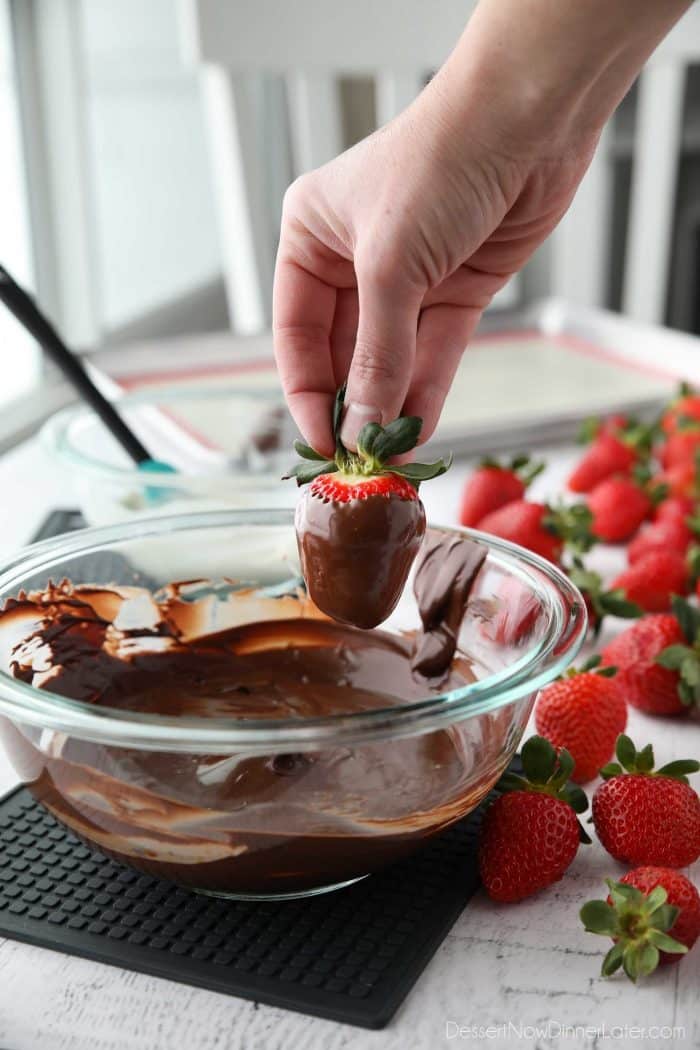 To dip a strawberry in chocolate: Hold the strawberry firmly by the stem, dip it into the melted chocolate, twist/rotate the berry until fully coated, then let the excess chocolate fall back into the bowl, or lightly scrape the bottom on the side.