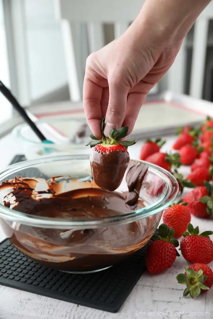 To dip a strawberry in chocolate: Hold the strawberry firmly by the stem, dip it into the melted chocolate, twist/rotate the berry until fully coated, then let the excess chocolate fall back into the bowl, or lightly scrape the bottom on the side.