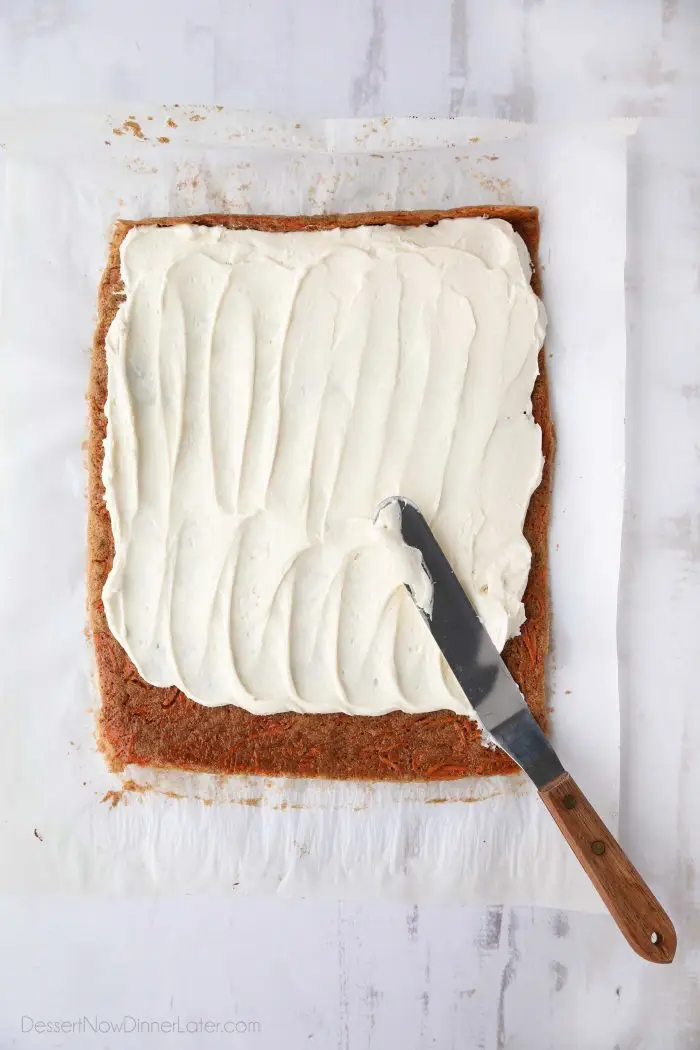 Cream cheese frosting being spread over a thin layer of carrot cake. 