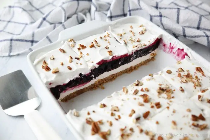 Squares of Blueberry Delight dessert show layers of graham cracker pecan crust, no-bake cheesecake, blueberry filling, and whipped topping.