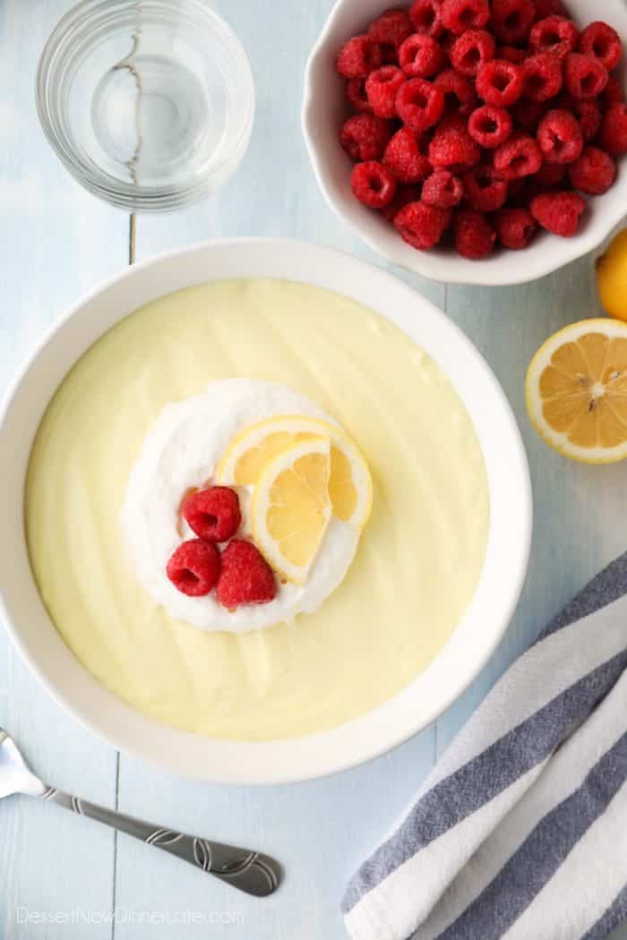 A big bowl of lemon jello salad is topped with whipped cream, raspberries, and lemon slices.