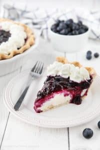 Slice of blueberry cream cheese pie on a plate with whipped cream on top.