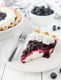 Slice of blueberry cream cheese pie on a plate with whipped cream on top.