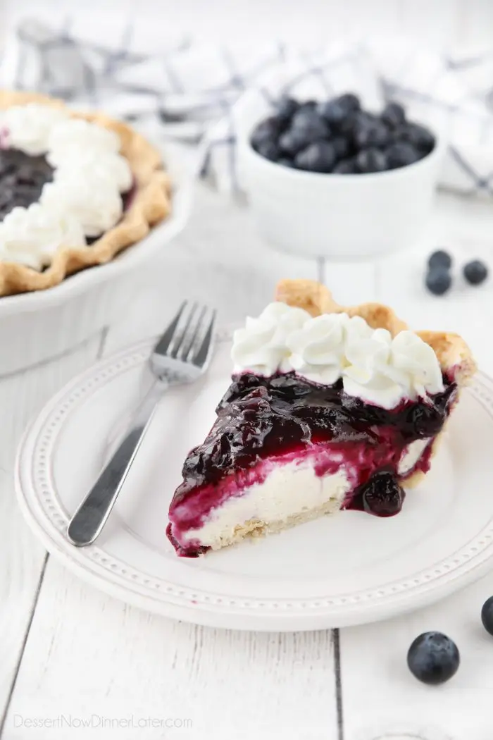 Slice of blueberry cream cheese pie on a plate with whipped cream on top.