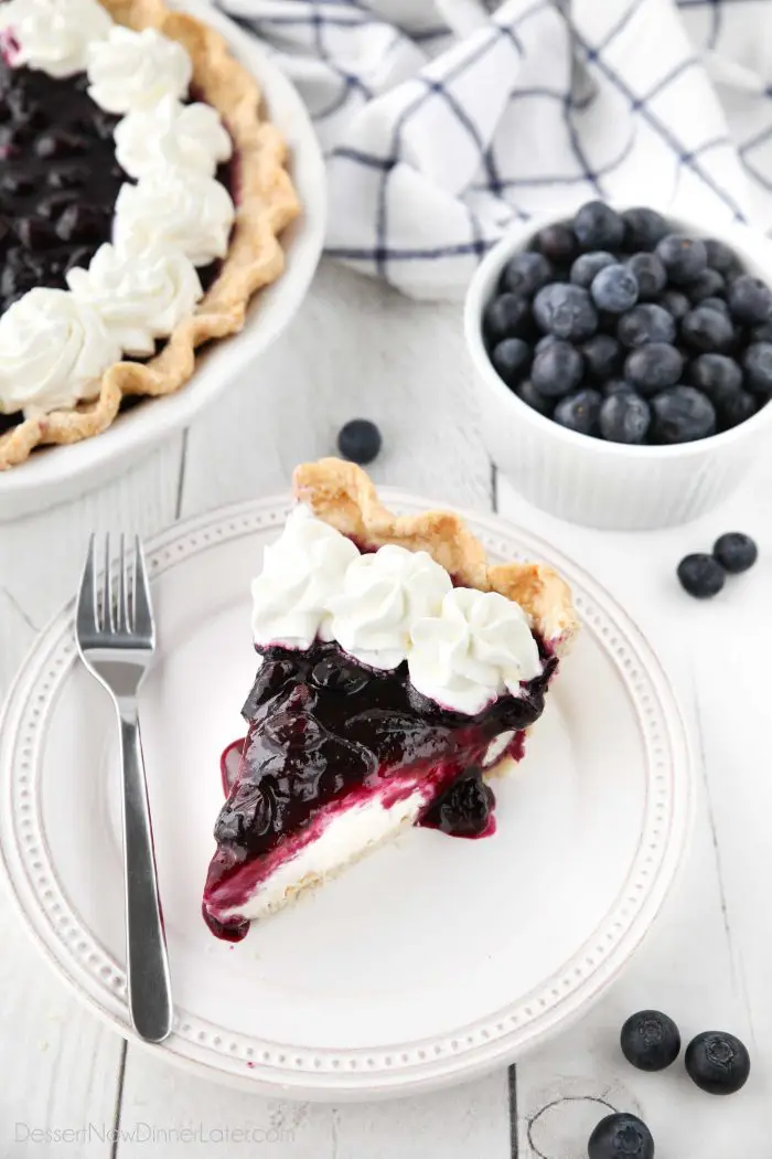 Slice of blueberry cream cheese pie on a plate with whipped cream on top.