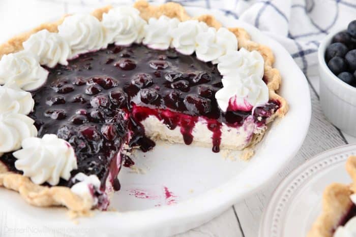 Blueberry Cream Cheese Pie with whipped cream on top and a couple slices missing from dish.