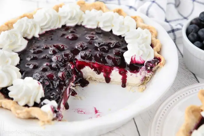 Blueberry Cream Cheese Pie with whipped cream on top and a couple slices missing from dish.