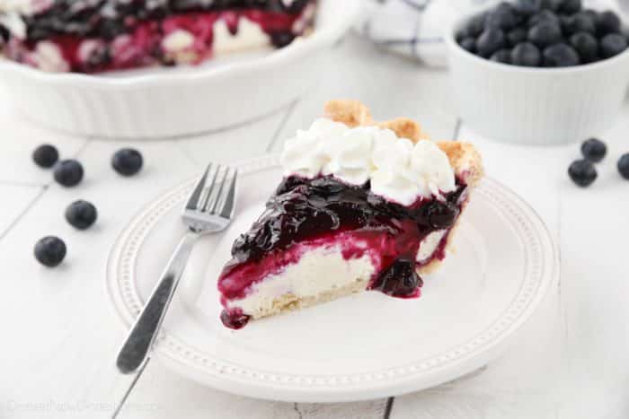 Slice of blueberry cream cheese pie on a plate with whipped cream on top.