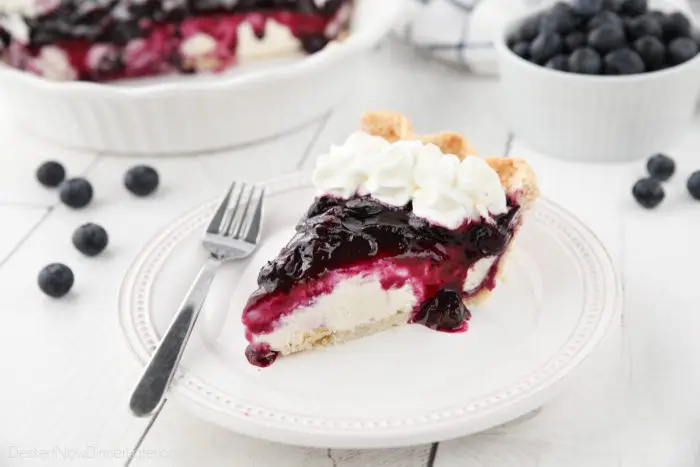 Slice of blueberry cream cheese pie on a plate with whipped cream on top.