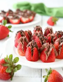 Plate of strawberries filled with no bake chocolate cheesecake filling and topped with mini chocolate chips.