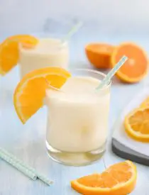 Orange Julius smoothie in a cup with a straw and fresh orange slices.