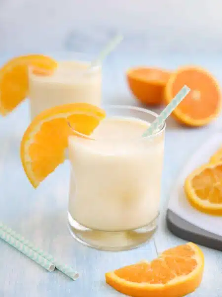 Orange Julius smoothie in a cup with a straw and fresh orange slices.
