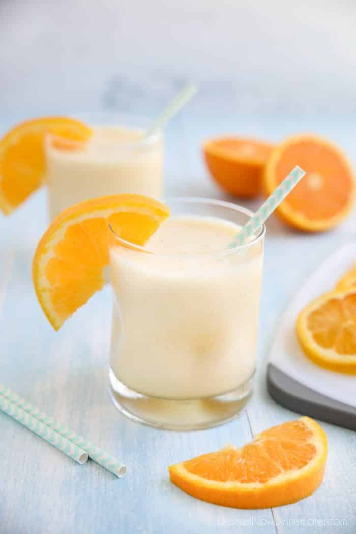 Orange Julius smoothie in a cup with a straw and fresh orange slices.