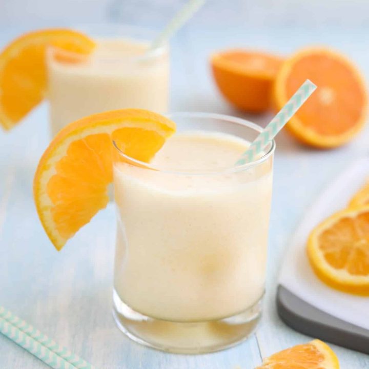 Orange Julius smoothie in a cup with a straw and fresh orange slices.