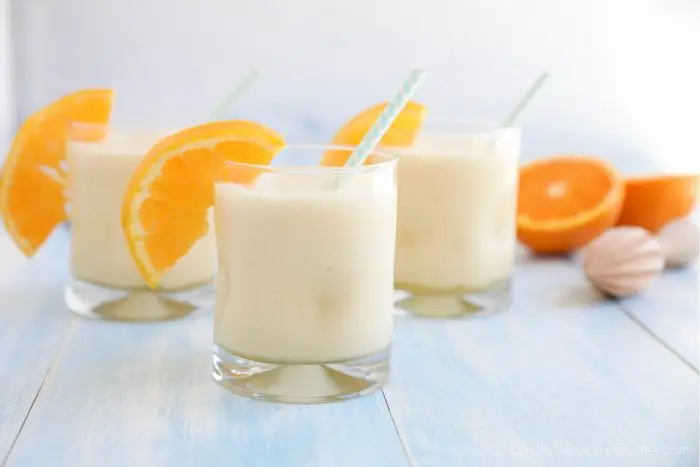 Orange Julius smoothies in cups with straws and fresh orange slices.