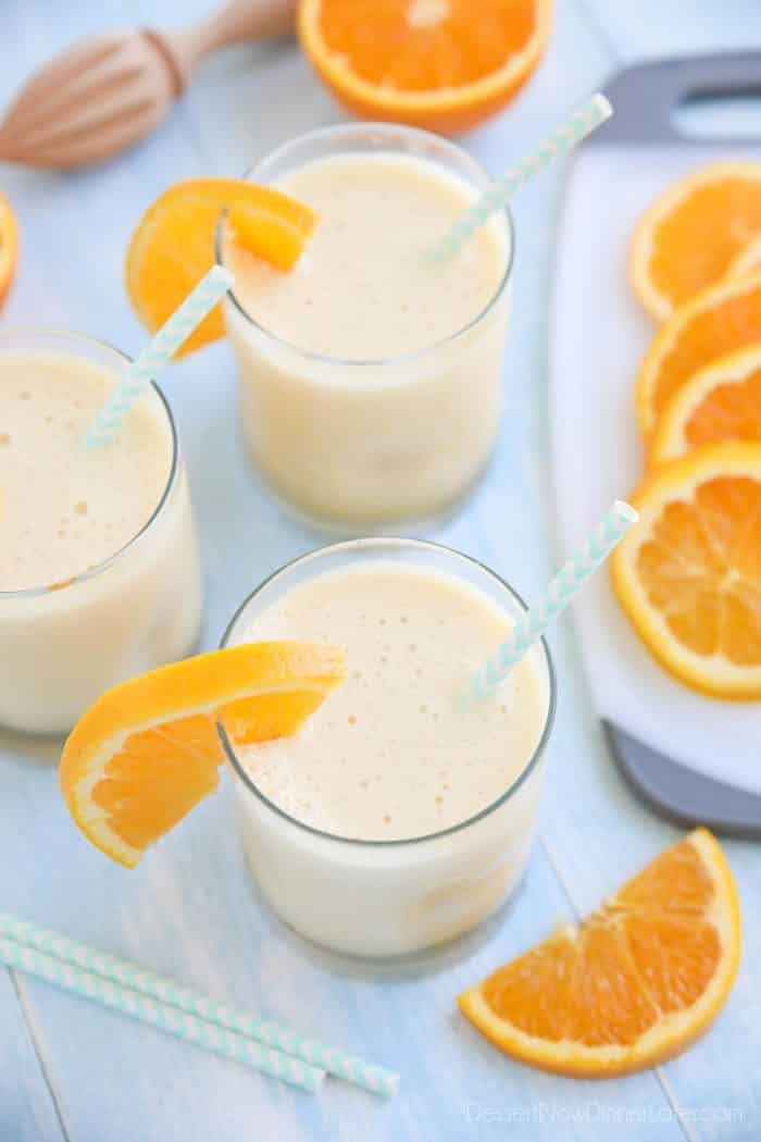 Orange Julius smoothies in cups with straws and fresh orange slices.