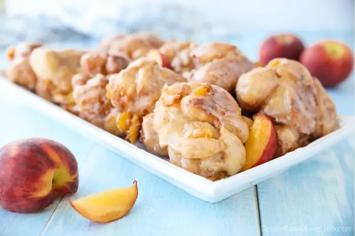 Glazed Peach Fritters Donuts on a platter with fresh peaches.