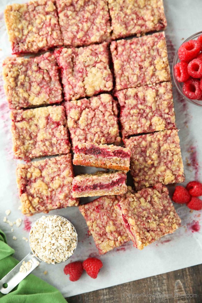 Raspberry Crumble Bars on parchment paper with fresh raspberries and oats.